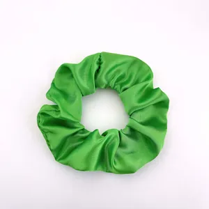 Detailed close-up of emerald green satin scrunchie showing smooth silk-like fabric texture