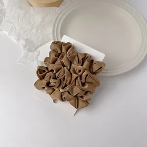Detailed view of a brown satin scrunchie with smooth texture on a white display card