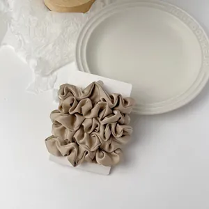 Macro detail of a champagne satin scrunchie with silk-like texture on a white display card