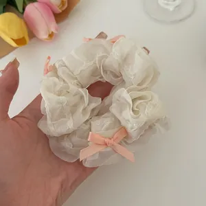 Detail of cream organza scrunchie featuring pink ribbon bows and delicate wavy edges