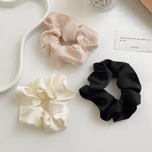 Detailansicht von drei Haar-Scrunchies aus Seidensatin in Creme, Nude-Rosa und Schwarz