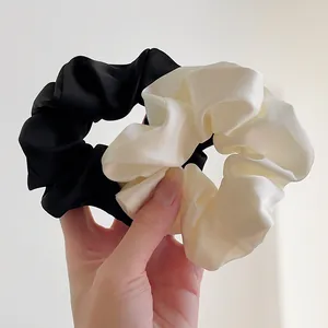 Nahaufnahme eleganter Scrunchies aus Satin in Schwarz und Beige mit seidigem Glanz