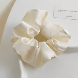 Detailaufnahme eines cremeweißen Satin-Haargummis auf einem dekorativen weißen Tablett