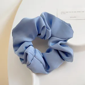Detailansicht eines staubblauen Satin-Haargummis mit Seidentextur und eleganten Falten