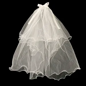 Détail du voile de mariée blanc multicouche avec nœud et bords ondulés sur fond noir