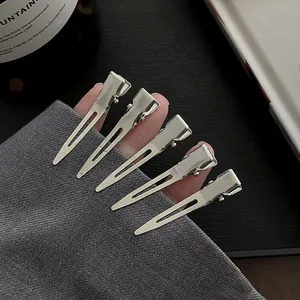 Detailed close-up of five silver metal duckbill clips held by a model for hair styling