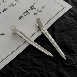 Close-up of two silver metal hair clips with hole designs on a black and white background