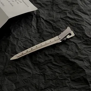 Polished silver metal hair sectioning clip with dot patterns on textured black background