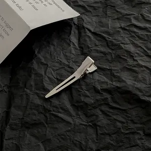 Detail of silver metallic duckbill hair clip on a textured black paper background