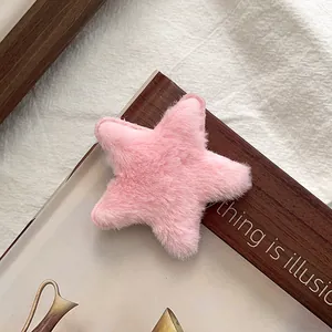 Détail d'une pince à cheveux étoile en peluche rose sur des magazines aux tons doux