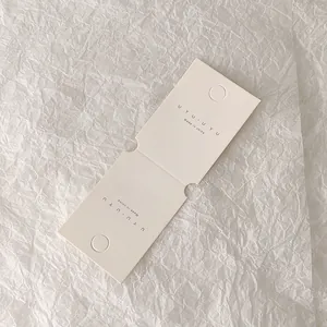 Detalle de cartón blanco roto para exhibir joyas con logotipo y agujeros de colgar