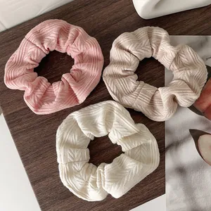 Detailed view of three knitted scrunchies in pink, beige, and cream with herringbone pattern