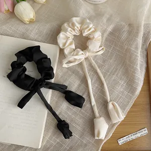 Detail of satin bow scrunchies with long ribbons and tulip charms in black and beige