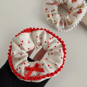 Detailed close-up of plush scrunchies featuring cherry prints and red bow accents