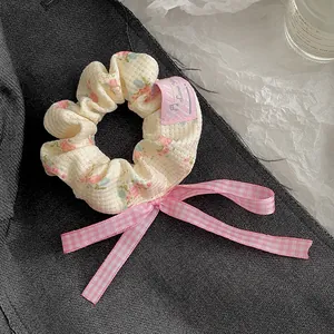 Detail eines Blumen-Haargummis mit rosa karierter Schleife auf beigem Stoff