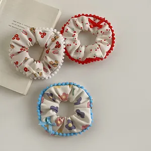 Detailed shot of three plush floral hair scrunchies with pom-pom edges and cute bows