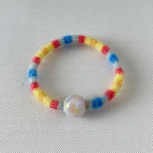 Détail d'un élastique à cheveux tricoté arc-en-ciel avec une perle blanche lisse