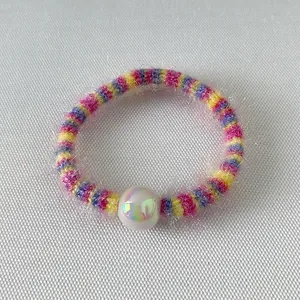 Détail d'un élastique arc-en-ciel en tricot pelucheux avec une perle blanche nacrée
