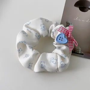 Détail du chouchou blanc à motifs ours avec nœud rose et bouton cœur bleu décoratif