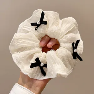 Detailansicht eines cremefarbenen Spitzen-Scrunchies mit schwarzen Schleifen und Perlen