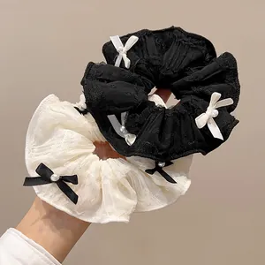 Nahaufnahme der Spitzen-Scrunchies mit zarten Schleifen und Perlen in Schwarz und Creme
