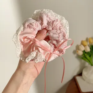 Detail van roze satijnen scrunchie met witte kanten rand en decoratief strikje van lint