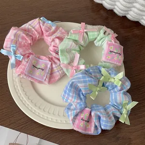 Detailed view of three checkered scrunchies with ribbon bows and handmade labels