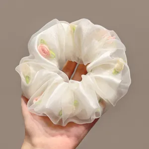 Détail d'un chouchou en organza blanc avec fleurs en tissu rose et feuilles vertes