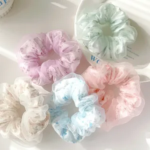Dettaglio di cinque scrunchie in organza floreale con pieghe morbide e mesh
