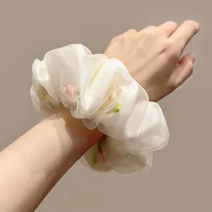 Détail du chouchou en organza blanc avec roses roses au poignet sous lumière douce