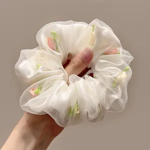 Détail de chouchou en organza crème avec bourgeons roses et feuilles vertes