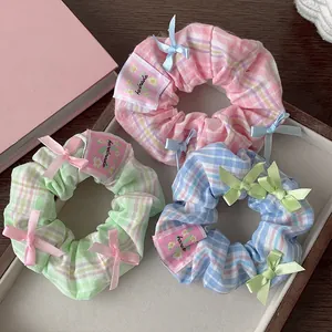 Detailed shot of pastel plaid scrunchies with mini bows and handmade labels in a tray