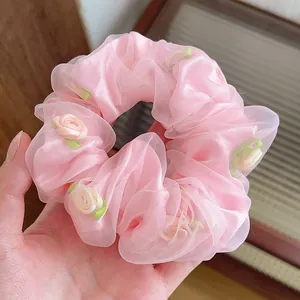 Détail du chouchou en organza rose avec roses faites main et feuilles vertes