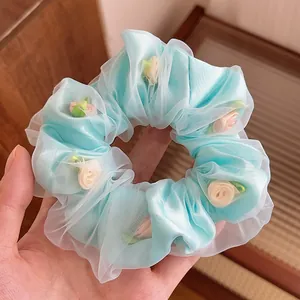 Détail d'un chouchou en maille bleu clair avec de délicats boutons de rose en tissu