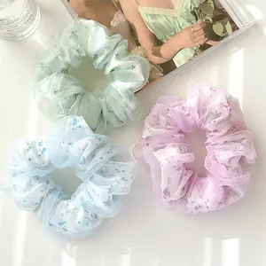 Dettaglio di scrunchies in organza floreale nei toni verde, viola e blu