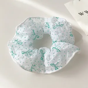 Detail eines weißen Haargummis aus Mesh mit grünen Punkten und Schleifenmuster