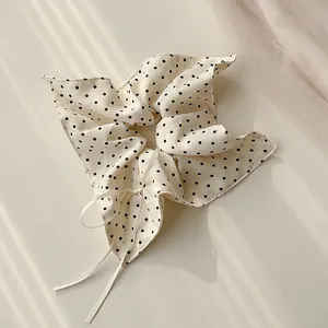 Dettaglio di uno scrunchie crema a pois neri con un nastro lungo effetto seta