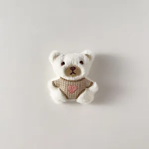 Dettaglio di orsetto di peluche crema con maglione marrone e ricamo a cuore rosa