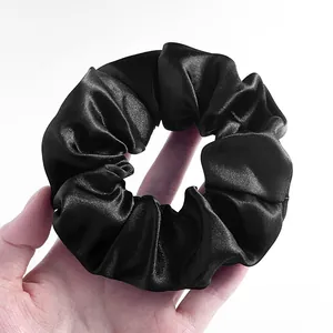 Detailopname van een zwarte satijnen scrunchie met glanzende textuur en plooien