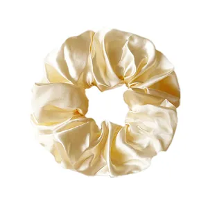 Detailed view of the champagne satin fabric texture and pleated design on this scrunchie