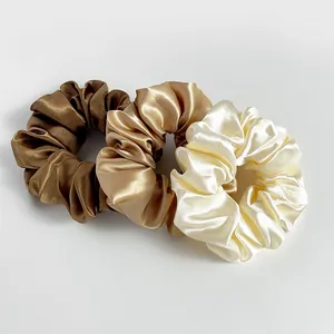 Gros plan de trois chouchous en satin dans les tons marron, doré champagne et blanc crème