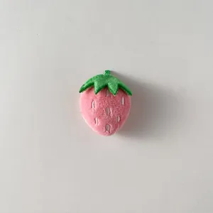 Dettaglio dell'accessorio fragola in peluche rosa con foglia verde e ricami bianchi