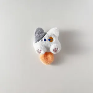 Dettaglio di un ciondolo a gatto in peluche bianco con orecchio grigio e base arancione