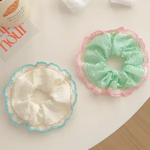 Detail of two lace-edged scrunchies in pastel green and white with delicate fabric texture