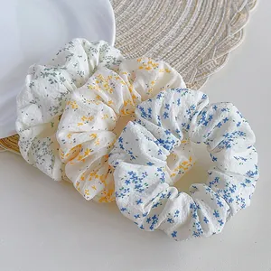 Close-up of three floral print scrunchies in green, yellow and blue on a white table