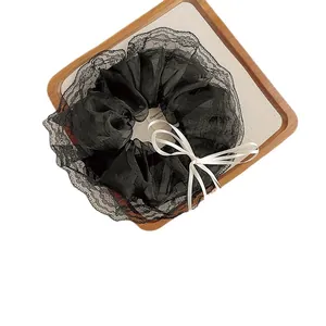 Elegant black lace mesh scrunchie with a cream ribbon bow on a wooden tray