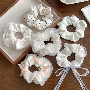Détail de chouchous en dentelle blanche avec nœuds et perles sur un plateau en bois