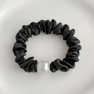 Détail d'un chouchou en satin noir élégant avec une grande perle blanche décorative