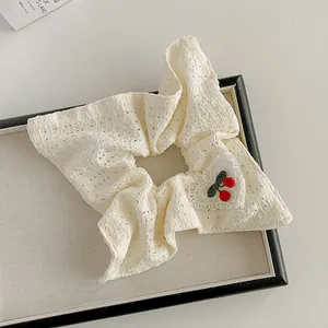 Détail du chouchou en dentelle blanche avec broderie cerise rouge sur un anneau en tissu