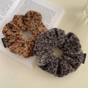 Brown and grey plush leopard print scrunchies with white embroidery on a book background